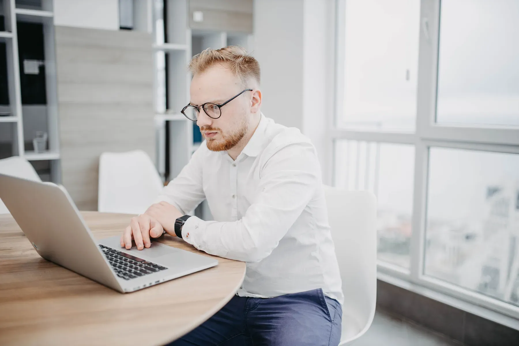 A professional working at a laptop in a day office with a city view at Grand Water Offices.