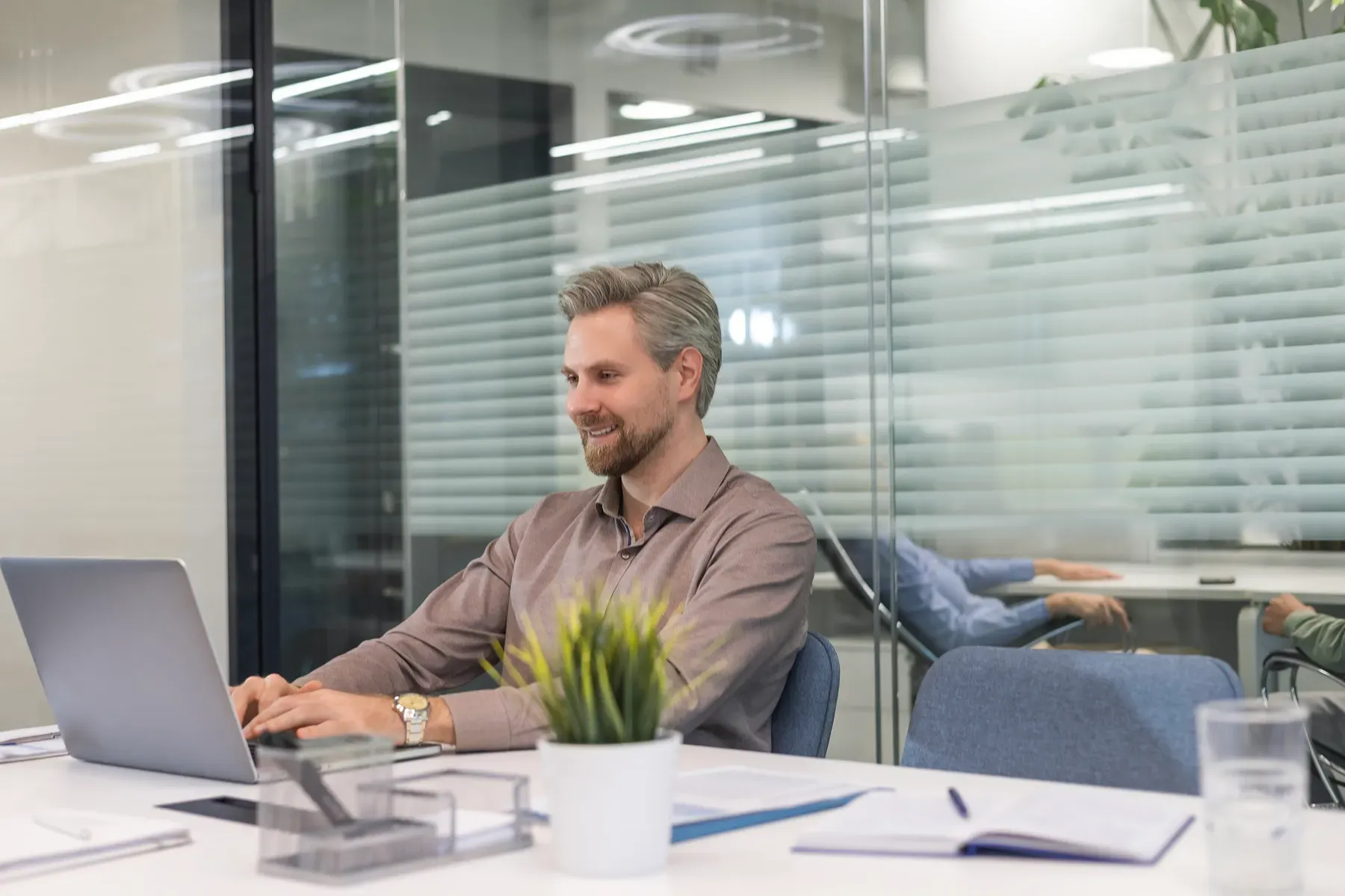 Colleagues meeting in a glass-walled meeting room at Grand Water Offices, natural light across the table.
